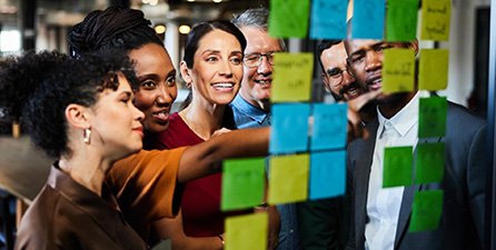 coworkers gathered around wall of sticky notes