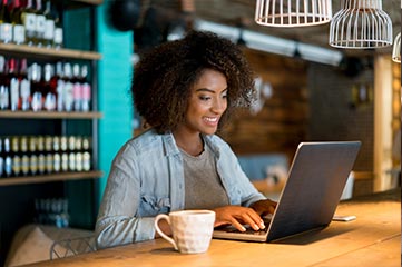 Mulher sorrindo na cafeteria usa compartilhamento de tela para colaborar do seu laptop