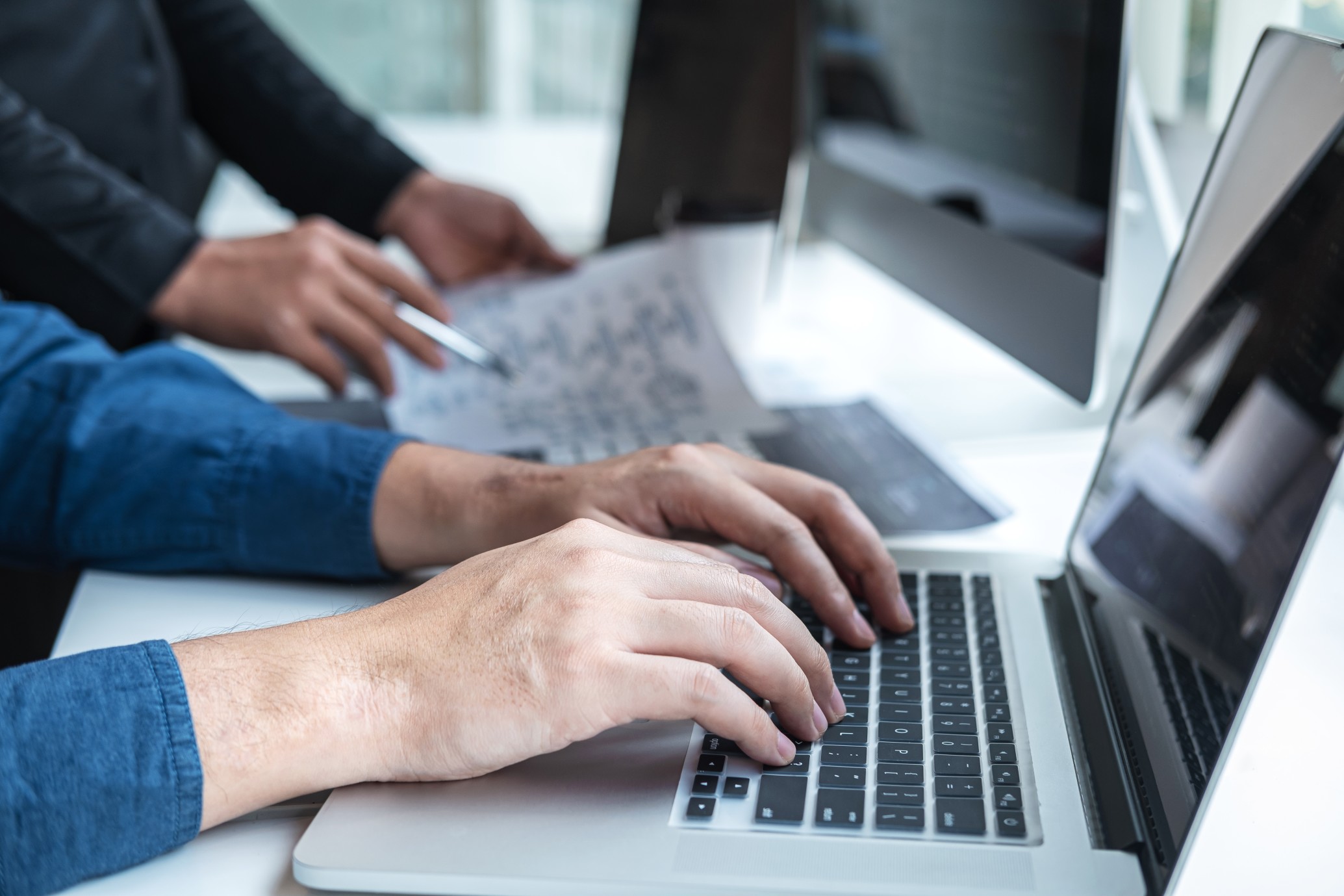 Een close-up van twee personen die aan het werk zijn op een laptop en een computer