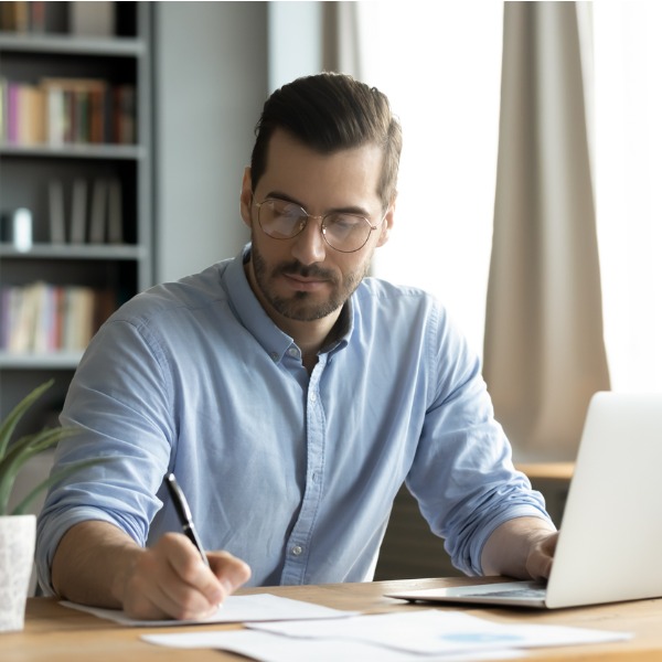 Man using laptop and taking notes by hand