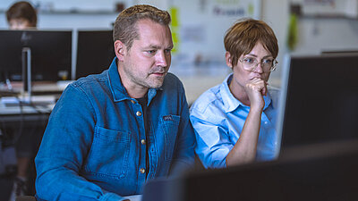 Two colleagues sit in front of a screen and brainstorm together