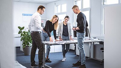 Colleagues standing in front of a table on which pictures are spread out and discussing their picture selection