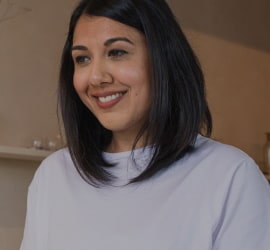 Mujer sirviendo té en una tetera en una cocina moderna, sonriendo y disfrutando del momento.