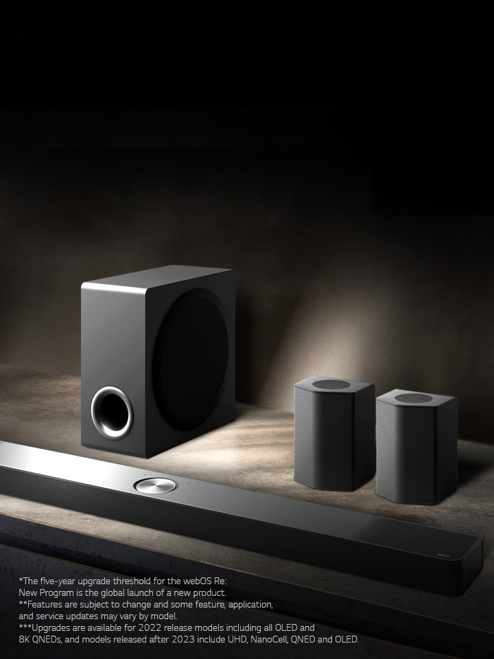 LG Soundbar, rear speakers, and subwoofer are placed within an angled perspective on a brown wooden shelf in a black room, enveloped in darkness with light only casting over the sound system.