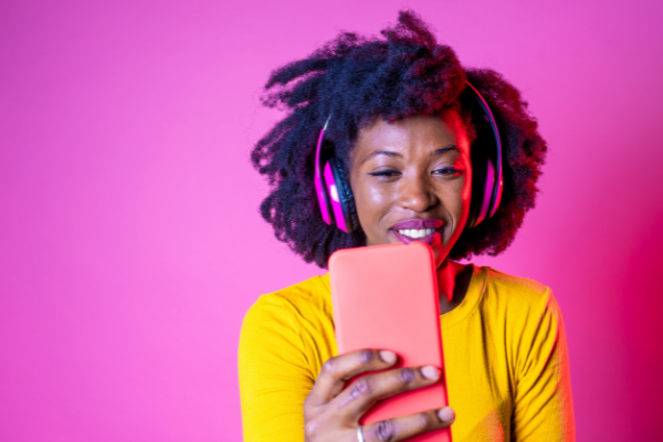 A guide to YouTube's algorithm 2023 - woman with headphones and phone in front of a pink background