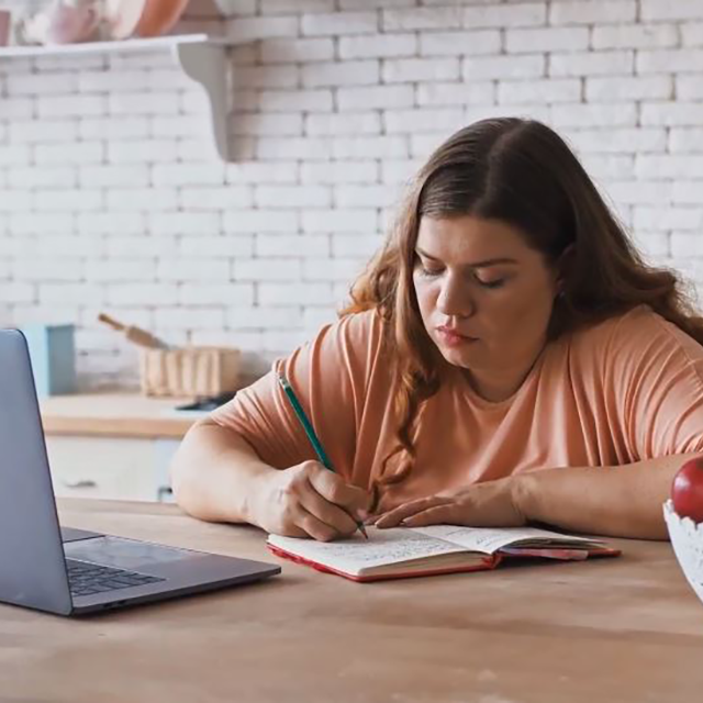 Woman taking notes in front of a laptop computer