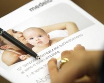 De hand van een vrouw rust op een Medela-boekje waaraan een pen is bevestigd.