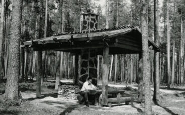 A man is sitting at the table at a campfire site in Petkeljärvi National Park, a black and white photo. 