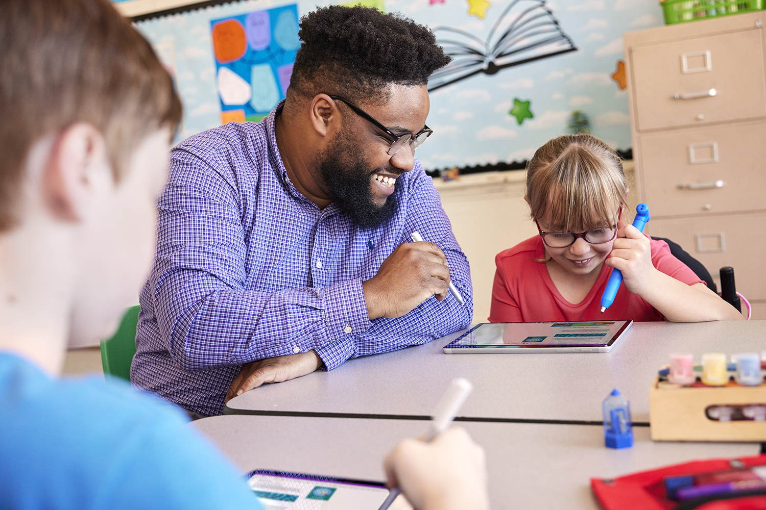 A teacher sitting with students, working together on a tablet.