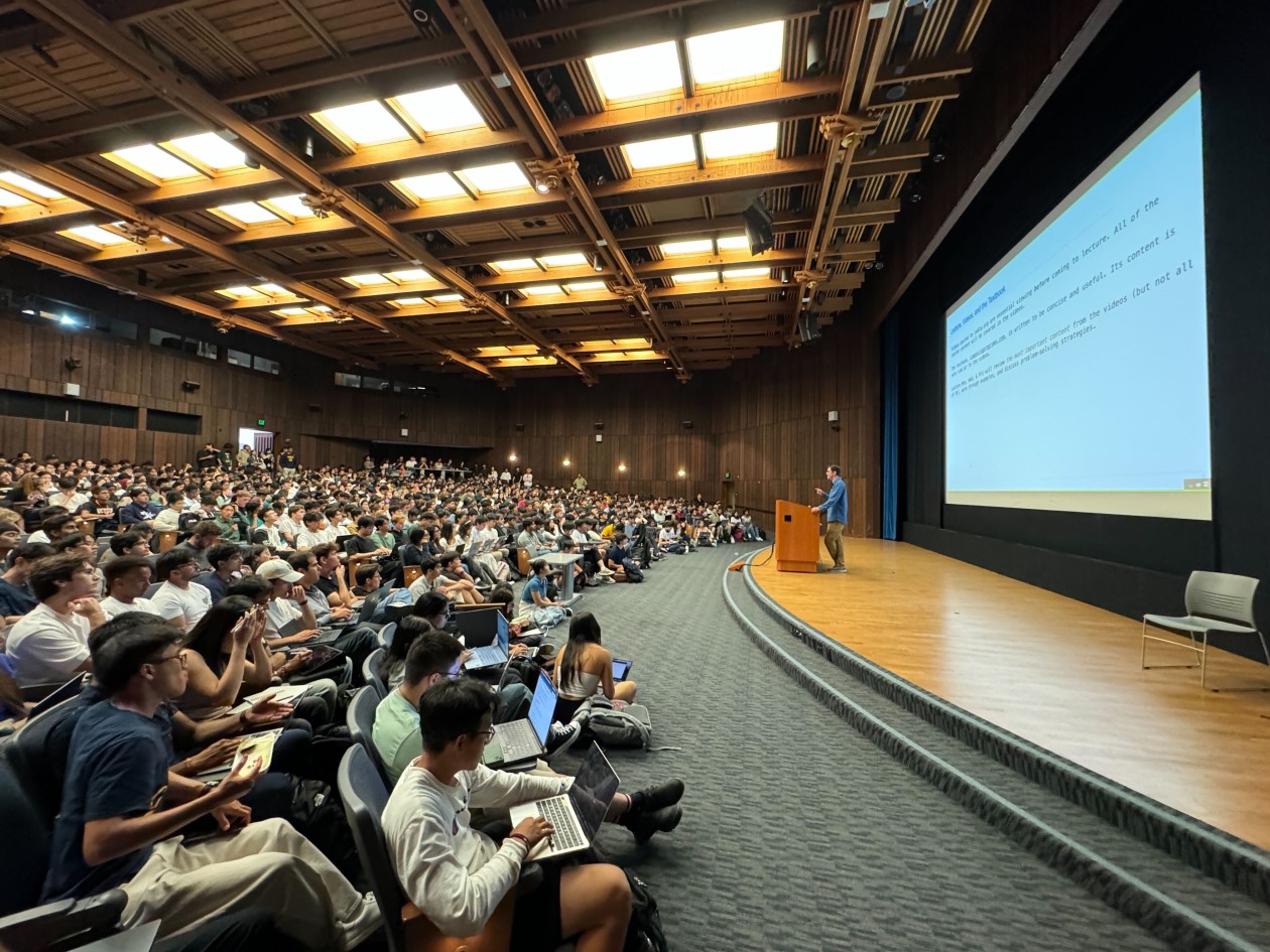 Decorative. A university professor standing at a podium and lecturing to an auditorium full of students.