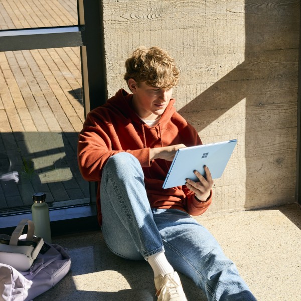 A university student sits on the floor while interacting with a tablet device.