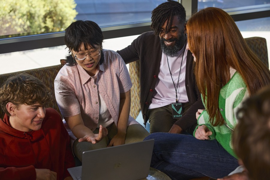 A group of higher education students and their professor looking at the screen of a laptop together.