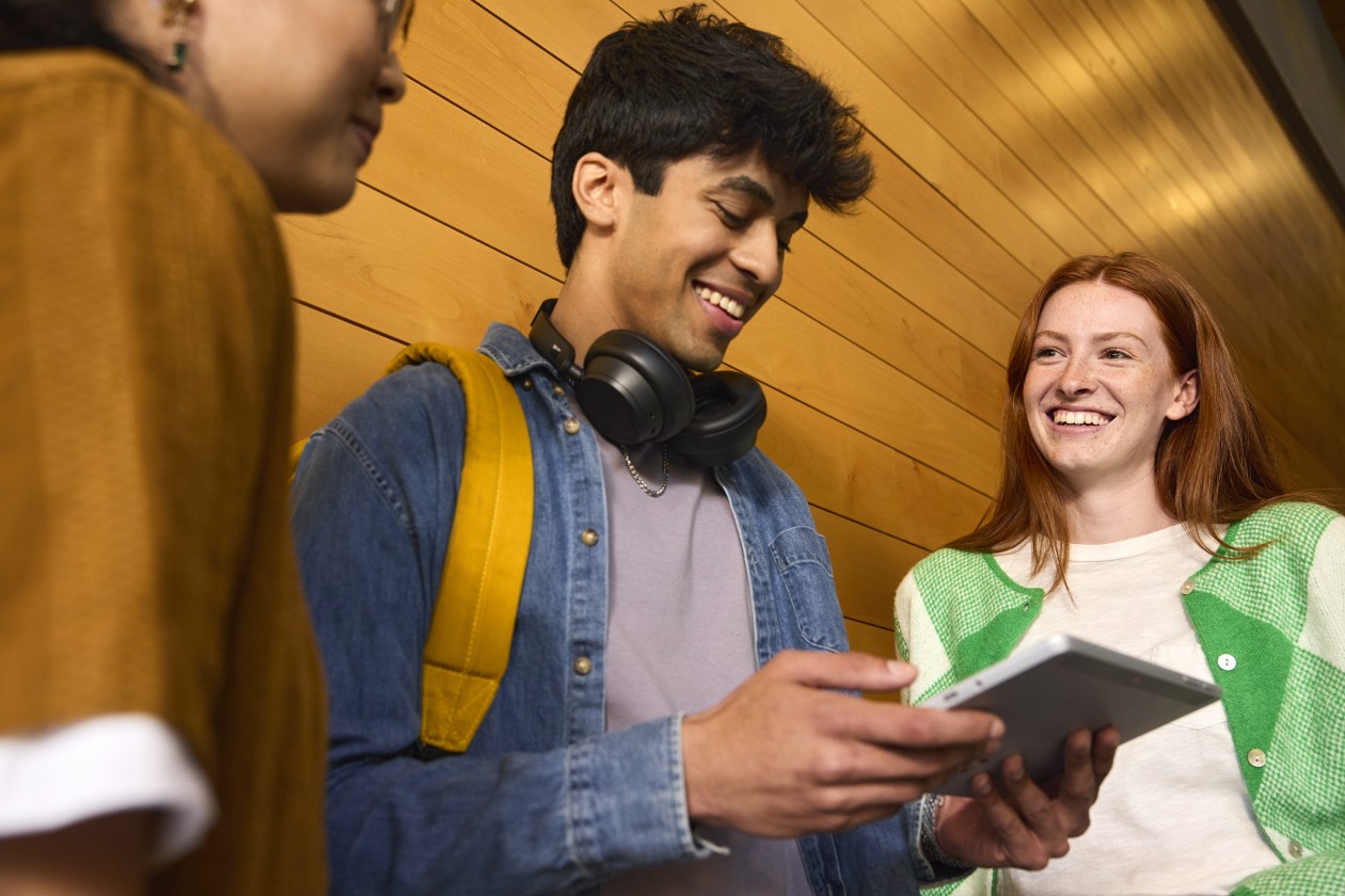 Students stand together in a university hallway gathered around a tablet device.