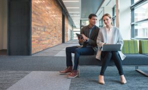 Image of two co-workers consulting one another on a bench outside a meeting room.