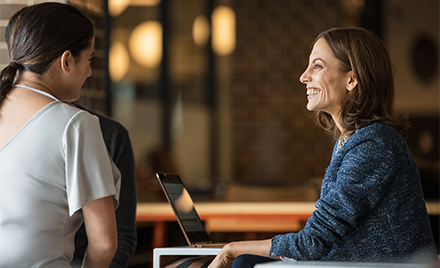 Image of two firstline workers meeting in a meeting room. One has her laptop open.