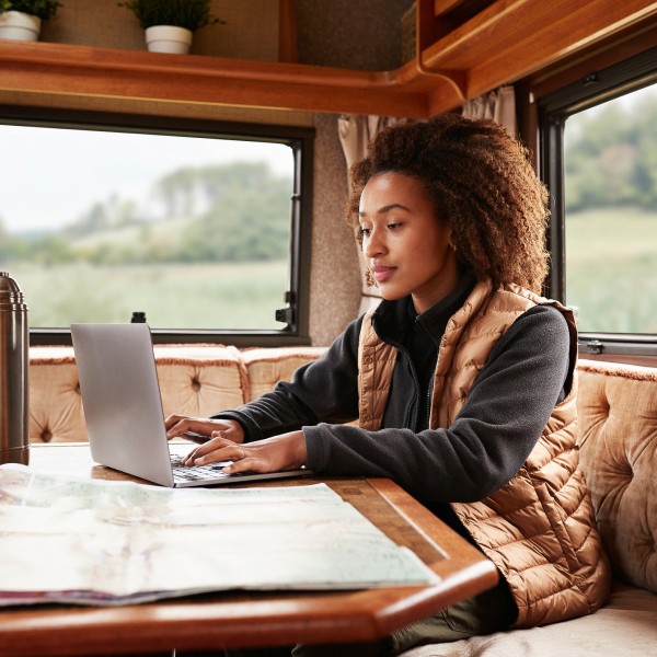 A young woman is smiling while working on her laptop, sitting comfortably inside a cozy camper van.