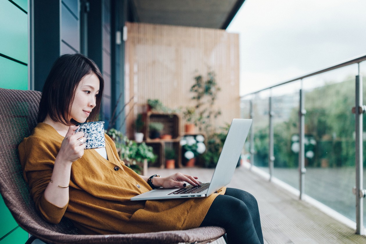 A young woman is working on her laptop on the balcony.