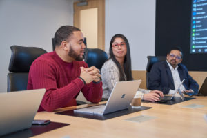 Group of people at a conference table with laptops who appear to be have a healthy and positive discussion or meeting.