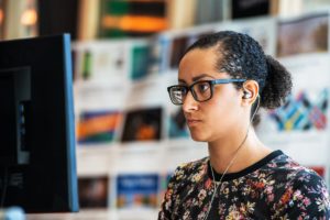 Adult woman works at computer station with headphones in.