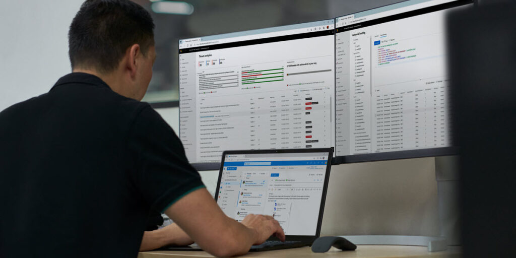 Security practitioner in front of two computer screens, working on their laptop to investigate threats.