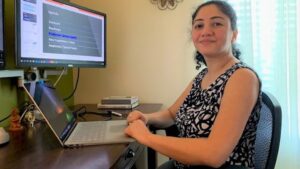 Bora sits at her desk in her home office. She is smiling as she looks off to the left toward the camera.