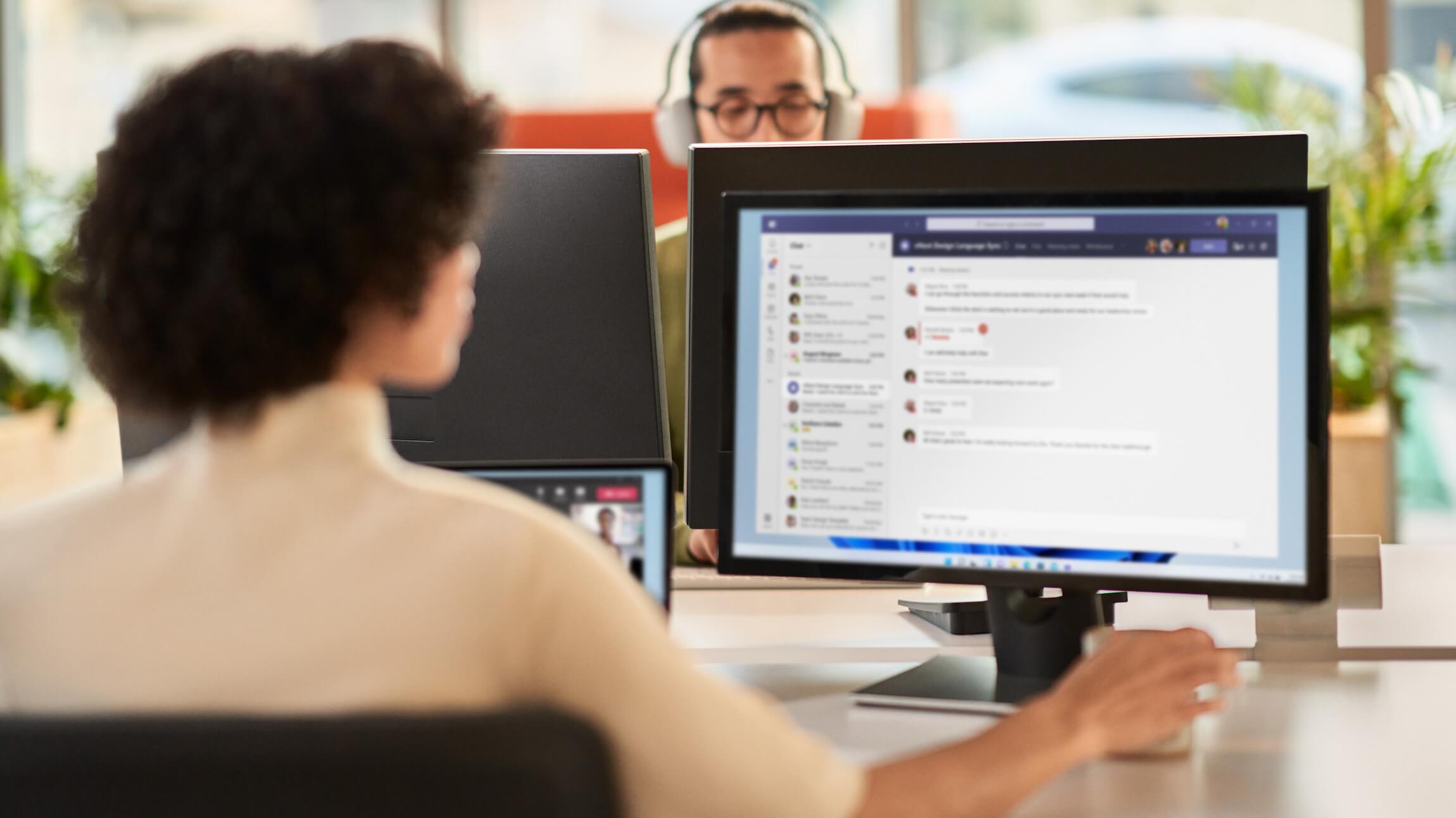 A woman collaborating during a Microsoft Teams meeting while working in an open office setting on dual monitor.