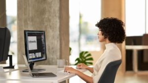 A woman collaborating with colleagues during a Microsoft Teams meeting while working in an open office setting.