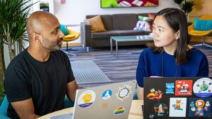 Zhou and Puttaswamy talk together while sitting in front of their laptops in an open space in a Microsoft office building.