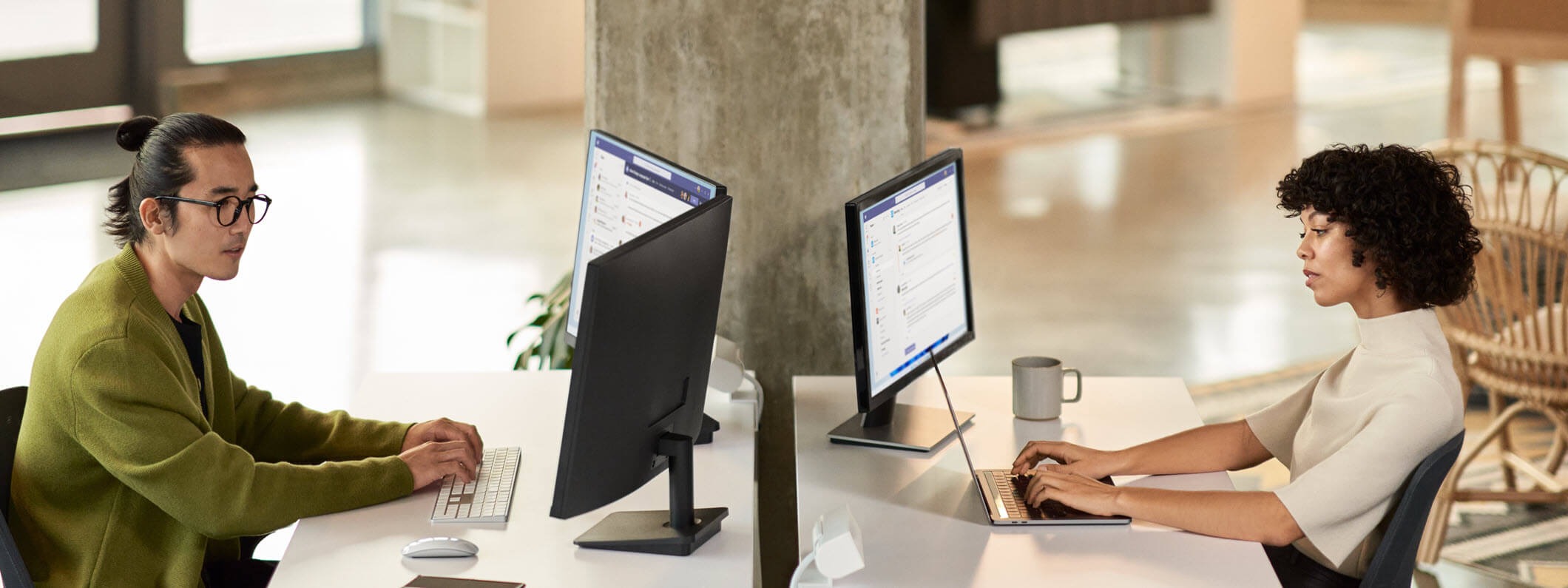 A man and a woman collaborating during a Microsoft Teams meeting while working in an open office setting on dual monitors.