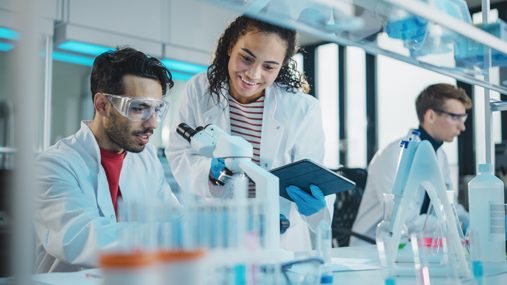 Three smiling young students working in a lab and looking at a microscope