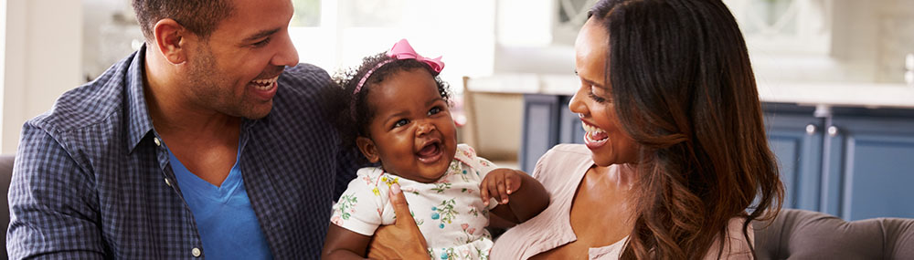 Two parents holding their infant between them and smiling. 