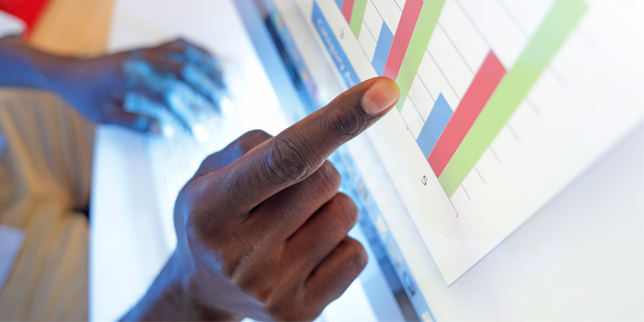 Close-up of a hand pointing to a bar graph displayed on a computer monitor. 