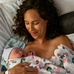 Infant resting on the bare chest of a caregiver under a blanket.