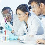 Three scientists wearing goggles looking at a test tube.