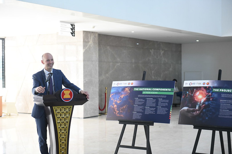 A man in formal wear speaks behind a podium with the PEEB ASEAN symbol