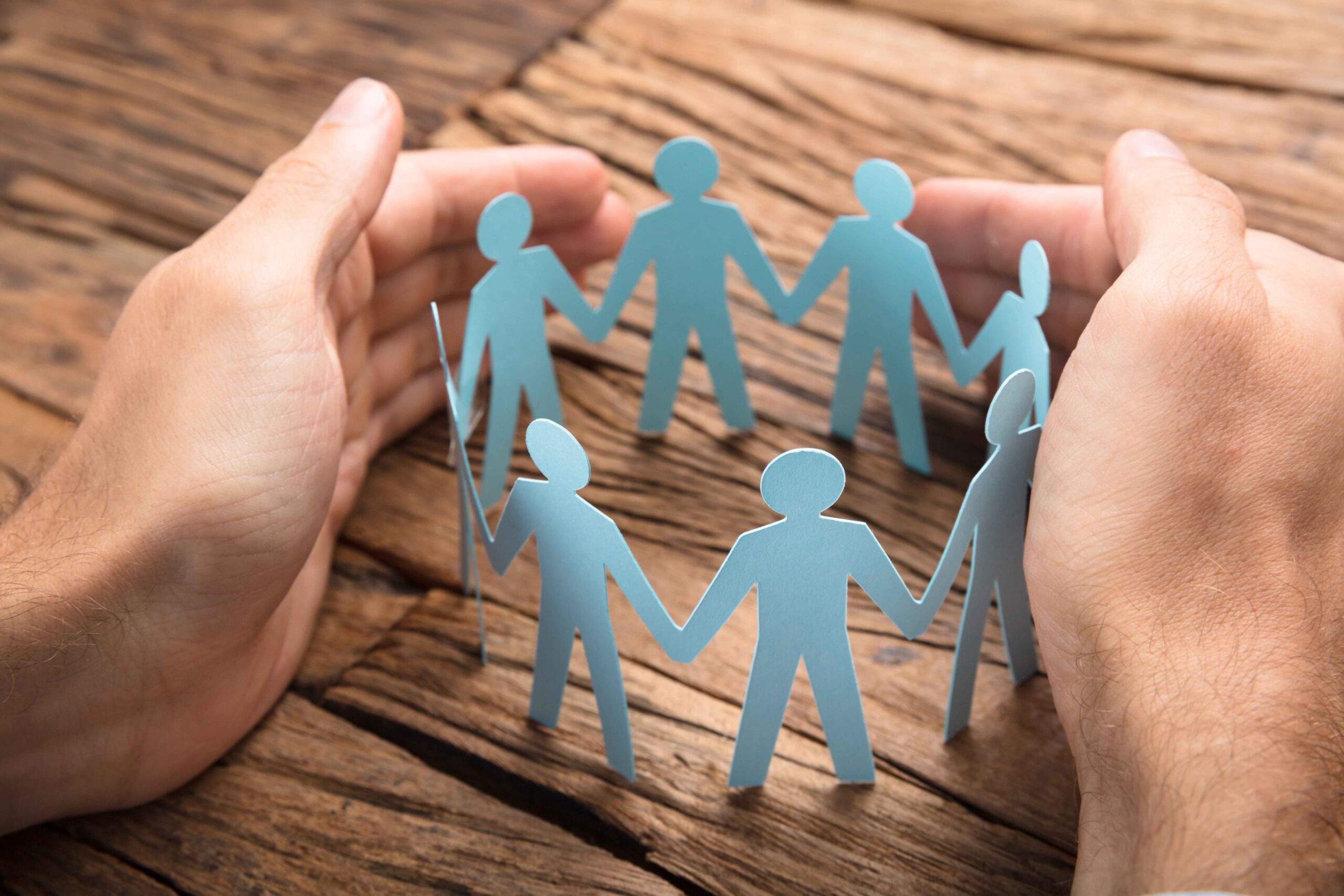 Businessman's Hands Covering Paper Team On Table