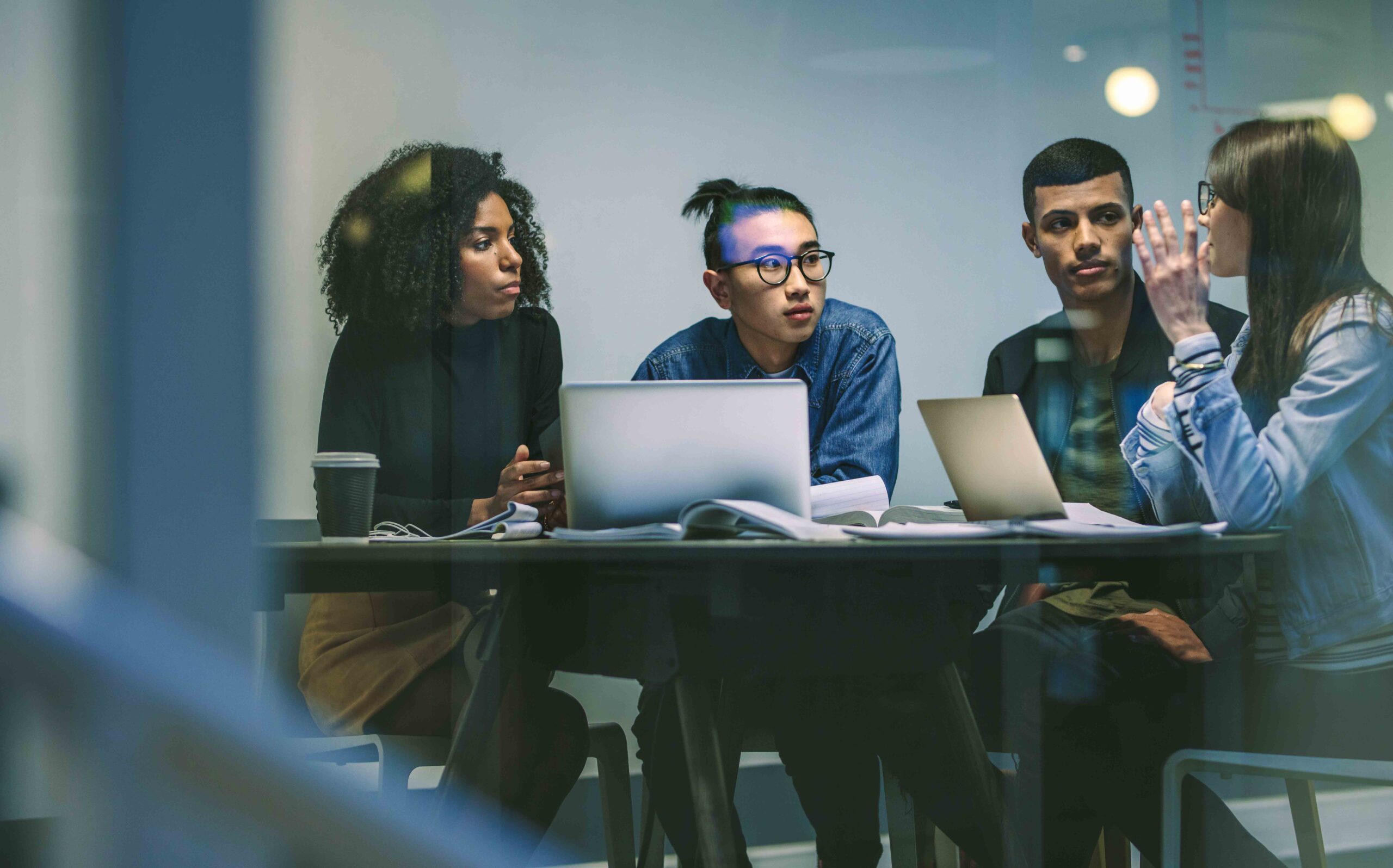 Woman talking with classmates while studying together around table. Young people sitting at the table working on an assignment.