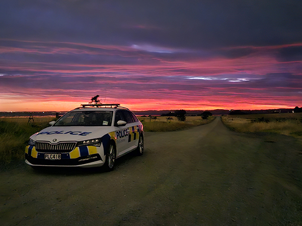 A police car parked at the side of a road in front of a dramatic sunrise. 