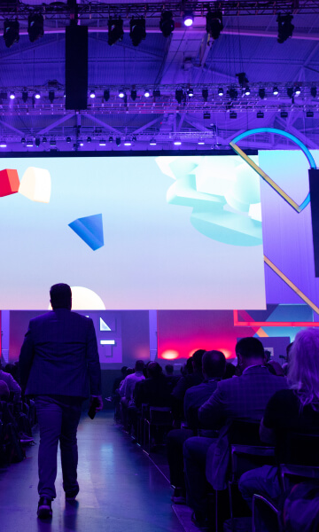 photograph of the audience at Red Hat Summit and a speaker walking toward the stage