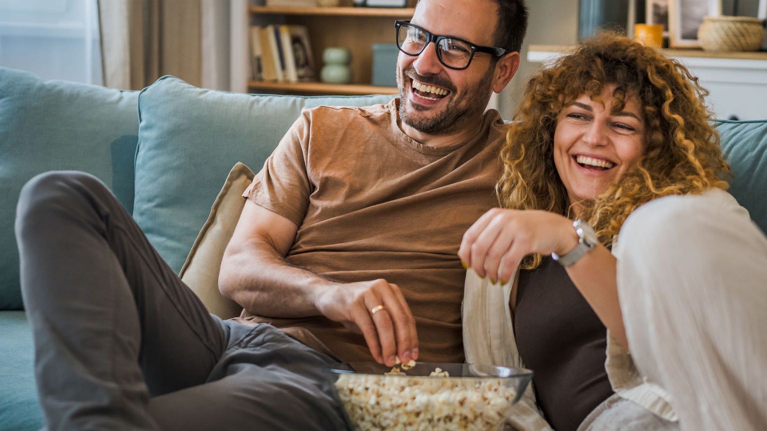 Couple sit at home on sofa bed streaming TV with Sonic Fiber Internet.