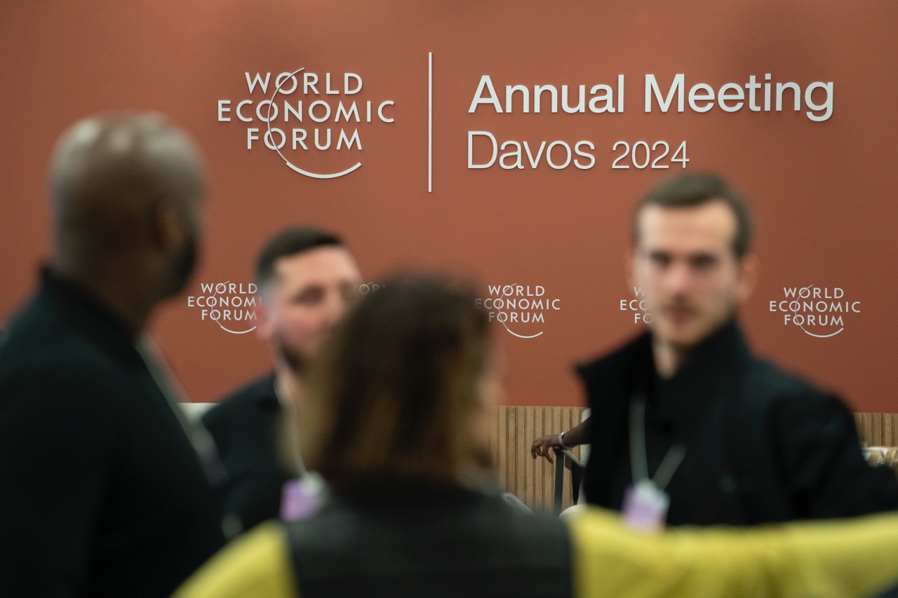 Group of people in foreground out of focus with Annual Meeting Davos 2024 background in focus.