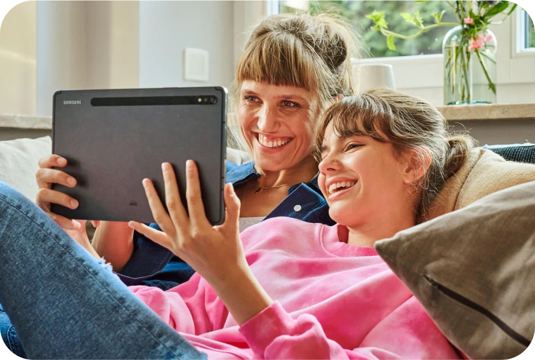 Mutter und Tocher schauen gemeinsam auf ein Tablet und genießen das schnelle Internet mit MagentaZuhause