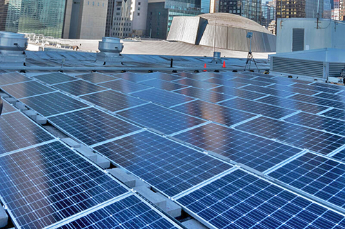 Solar panels being installed on roof of the United Nations with General Assembly building in background.