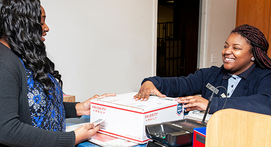 Person drops off Priority Mail package to USPS retail associate at a Post Office counter.