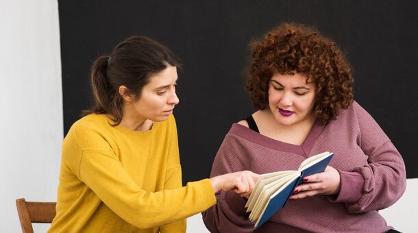 Eine Ehrenamtlerin hilft einer Frau beim Lesen lernen