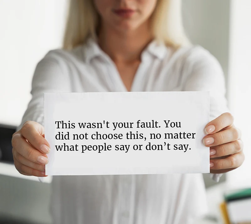 Woman holding note that reads This wasn't your fault. You did not choose this, no matter what people say or don't say.